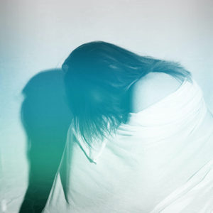 Image of a woman withdrawn and crouching with a blanket wrapped around her.