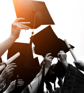 Picture of arms extended toward the sky holding diplomas and graduation caps