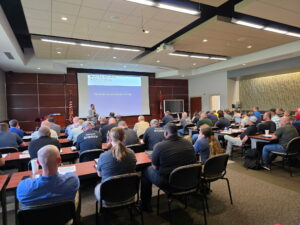 Picture of law enforcement officers seated in a large classroom looking at a large projection screen